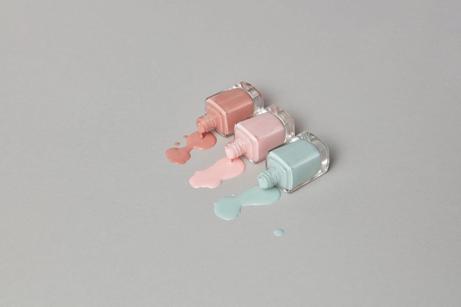 Several nail polish bottles in neutral shades arranged on a pale surface